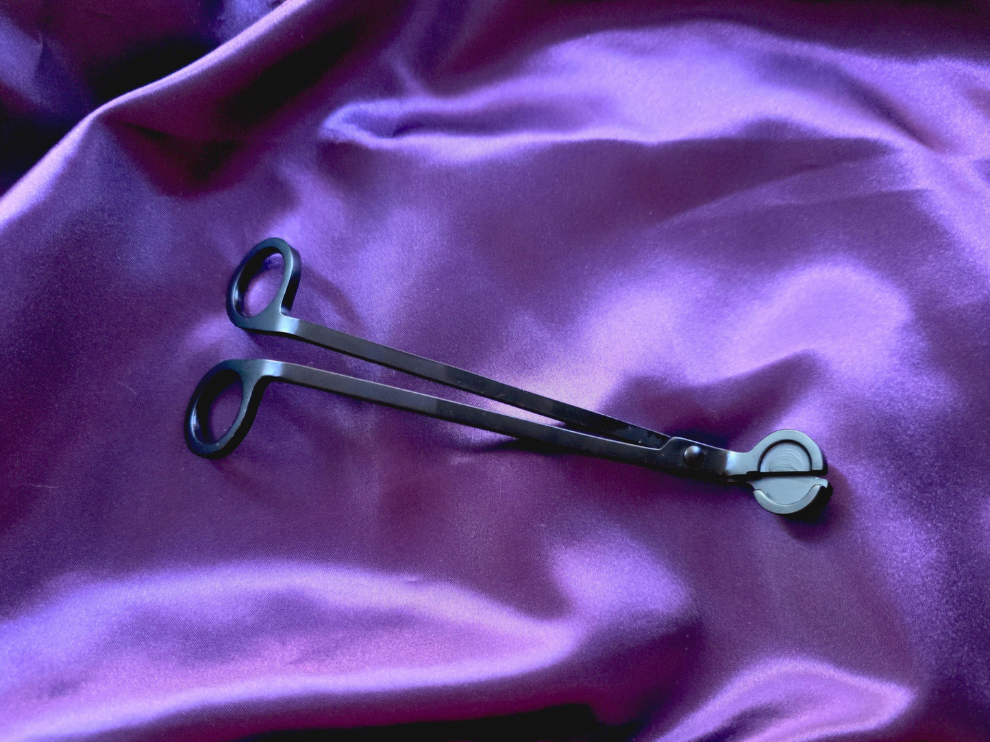 Metal wick trimmer on a purple fabric background